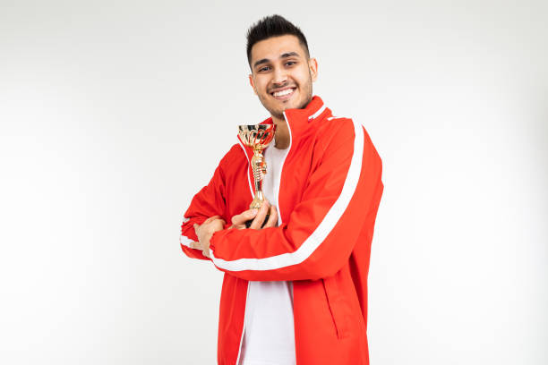 istock man in a red tracksuit shows off the winner's gold cup on a white background 1303630859