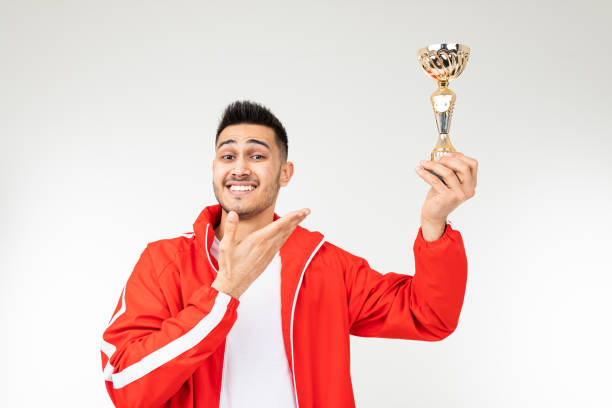istock man in a red tracksuit holds a winner's gold cup raised up on a white background 1303630864