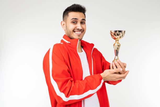istock happy athlete in tracksuit with a golden winner cup on a white studio background 1303630868