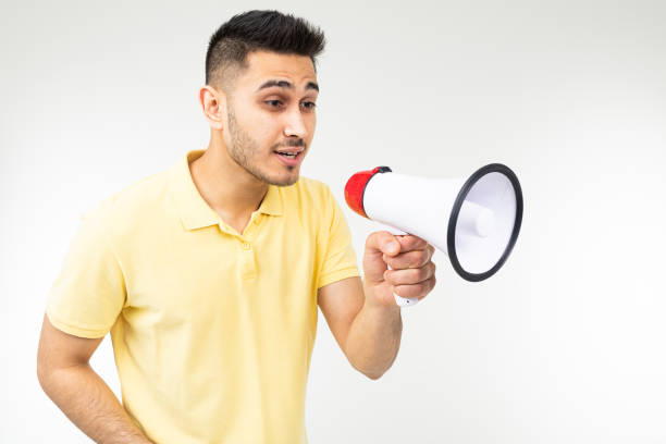 istock cool brunette man in a yellow T-shirt with a megaphone in his hands on a white studio background 1303630943