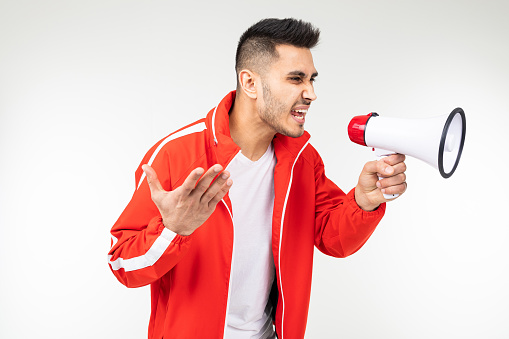 brutal man in a sports uniform shouting into a megaphone on a white studio background.
