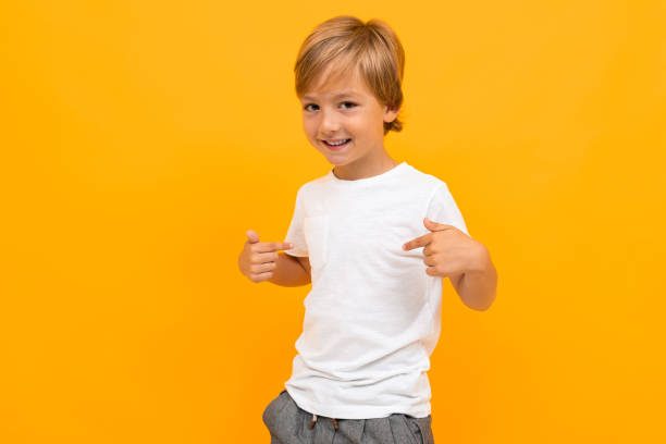 симпатичный маленький мальчик в футболке и брюках улыбается и показывает себя изолированным на желтом фоне - child little boys isolated standing стоковые фото и изображения