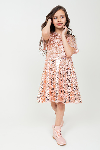 Full-length teenager girl in shiny party dress posing on a white studio background.