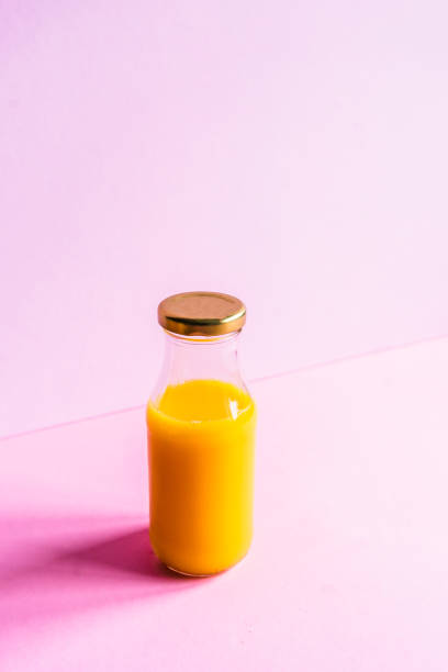 istock Orange juice in a glass bottle on a pink background 1303634732