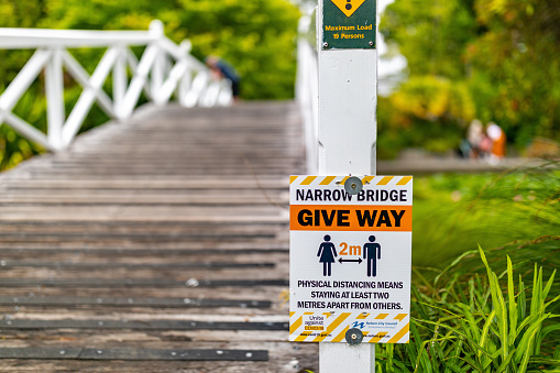 In this January 19, 2021 photo, a sign reminds visitors at the Queen's Gardens in Nelson, New Zealand to maintain 2 metres of distance from others on a footbridge. New Zealand has been praised for its strong handling of the COVID-19 pandemic.