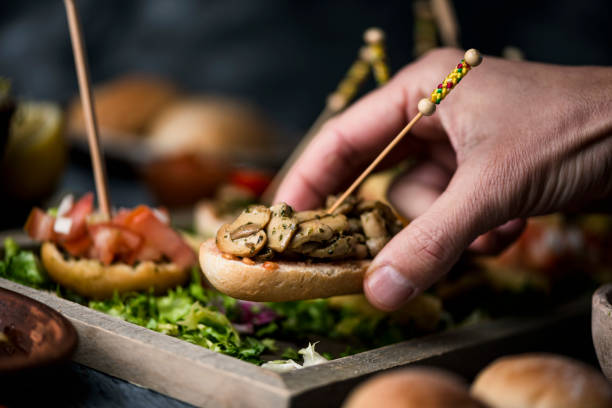 man takes a vegan spanish pincho a young caucasian man takes a vegan spanish pincho from a tray with some other pinchos, made with bread with different toppings, served as snacks or appetizers appetizer plate stock pictures, royalty-free photos & images