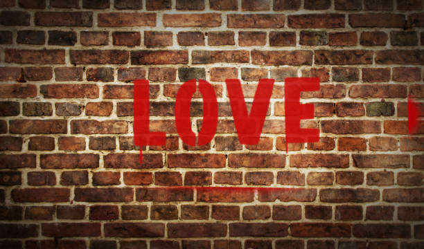 Love spray painted red inscription on the brick wall. Graffiti art concept of romantic emotion, happy couple and wedding. Urban abstract artwork. Airbrush paint.