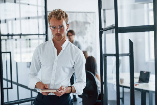 istock Man in glasses with notepad in hands stands in the office opposite employees 1303638039