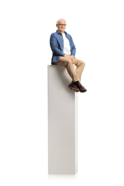 istock Smiling mature man sitting on a tall white post and smiling at camera 1303638861
