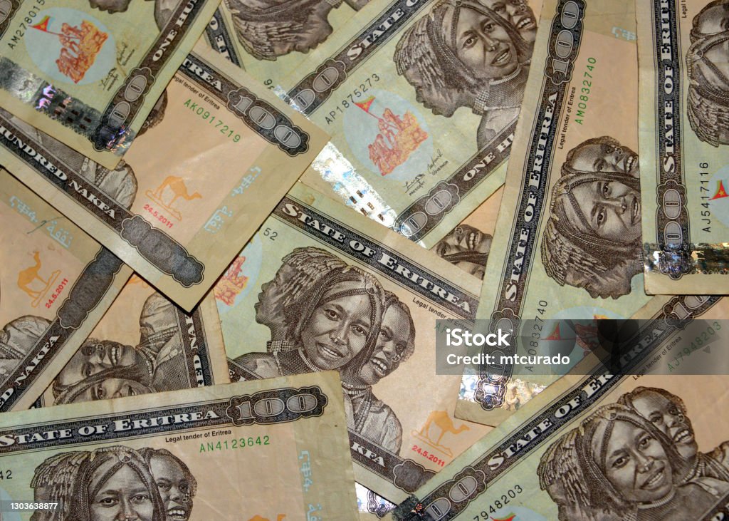 Eritrean nakfa bank notes - 100 ERN in random arrangement Asmara, Eritrea: Eritrean nakfa bank notes, currency of Eritrea, replaced the Ethiopian birr in 1997, pegged to the US dollar - named after the Eritrean town of Nakfa - 100 Nakfa notes display a triptych portrait of three young women of Eritrea's different nationalities and flag raising by soldiers - ISO 4217. Africa Stock Photo