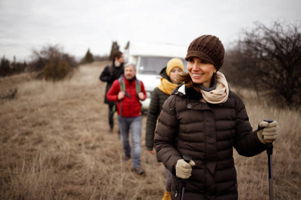 A family with two young adult children starts a hike on a cold winter day. They are walking away from their camper van parked on a field of dried grass.