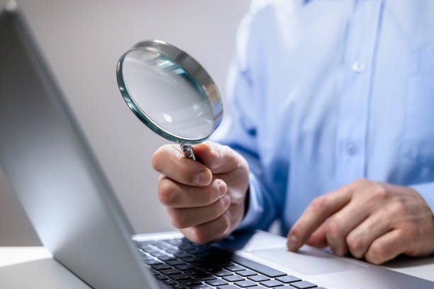 empresario con lupa leyendo documentos en línea en portátil - fine print fotografías e imágenes de stock