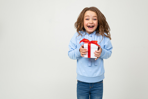 Front view of a cute little girl is holding a pink gift box in her hands with a nice smile in front of pure white background.