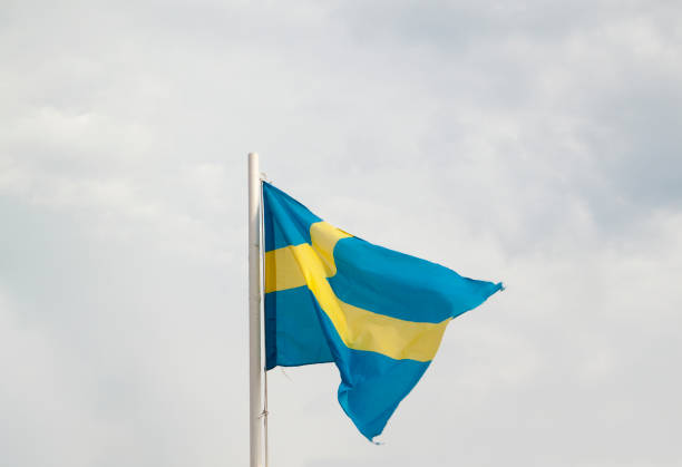 istock Flag of Sweden on a blue sky with clouds background 1303642373