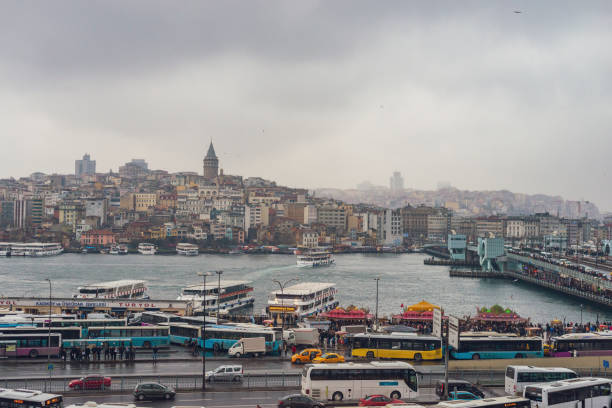 View fromt the Galata Bridge over Halic or Golden Horn, from the Bosphorus in Istanbul, Turkey on an overcast day. The Karakoy district with the Galata tower in the background. People are walking over the bridge.