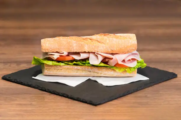 Photo of Select focus of a delicious looking meat and vegetables sub sandwich on a slate tray