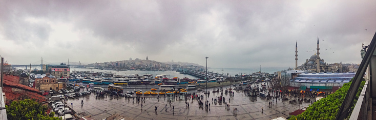 View over the Golden Horn and Bosphorus in Istanbul from the Fatih district on a rainy cloudy day. The Bus Station is on the left, the Galata Bridge (Galata Koprusu) is in the center of the panoramic photo and the New Mosque (Yeni Cami) on the right.