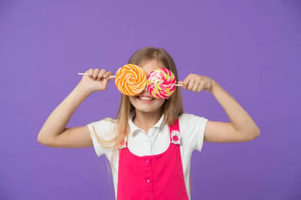 Funny child with lollipops on violet background. Girl smiling with candy eyes. Little kid smile with candies on sticks. Sweet look. Candyshop concept. Childhood and happiness. Having fun with candies