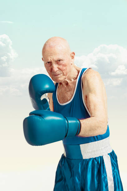 homme aîné utilisant la boxe de sportswear sur le fond de ciel. concept de sport, d’activité, de mouvement, de bien-être. copyspace, annonce. - boxing glove sports glove isolated old photos et images de collection