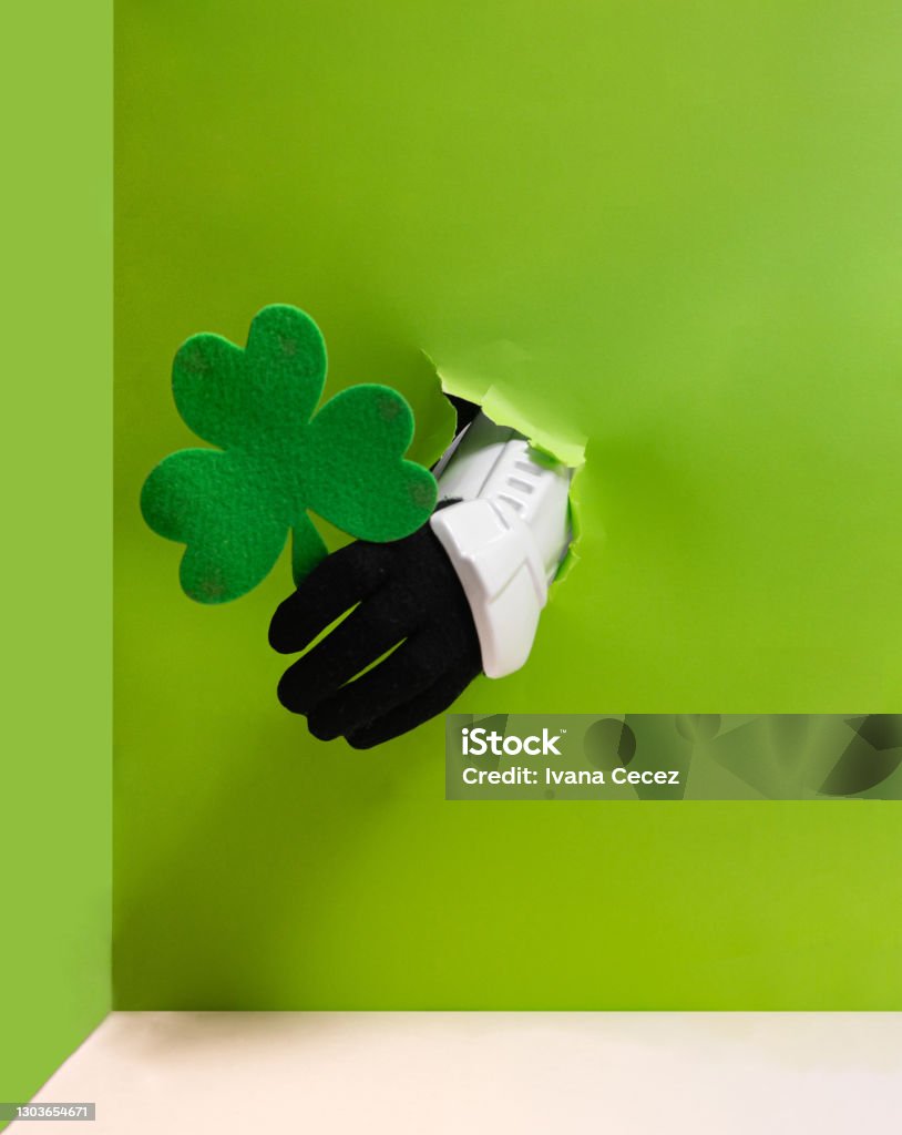 Storm trooper hand is holding green clover from bright green wall background. Abstract Stock Photo