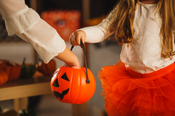 istock Woman putting candy in daughter's Jack o' lantern candy bucket 1303657652