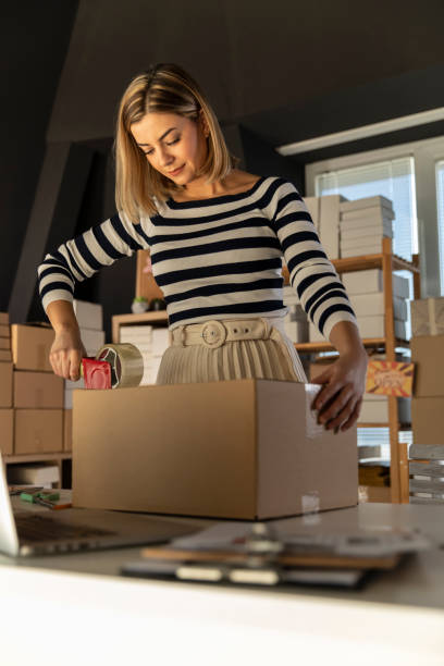 istock Diligent young woman taping a box with customer's order 1303660090