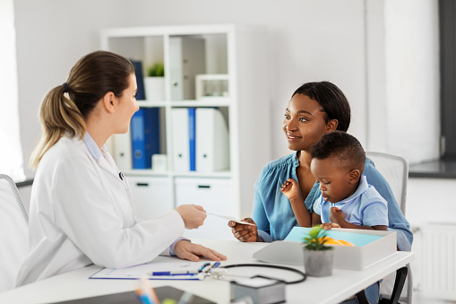 medicine, healthcare and pediatry concept - caucasian doctor giving prescription to african american mother with baby son at clinic