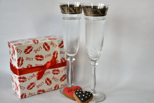 Two wineglasses, red and white Valentine's Day gift and heart-shaped gingerbreads lie on the holiday table.