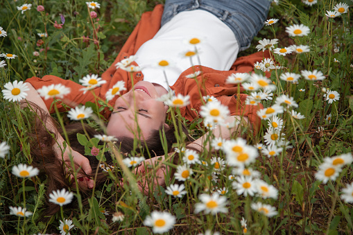 Beautiful girl with long brown hair in a white T-shirt lying in a chamomile field and smiling top view