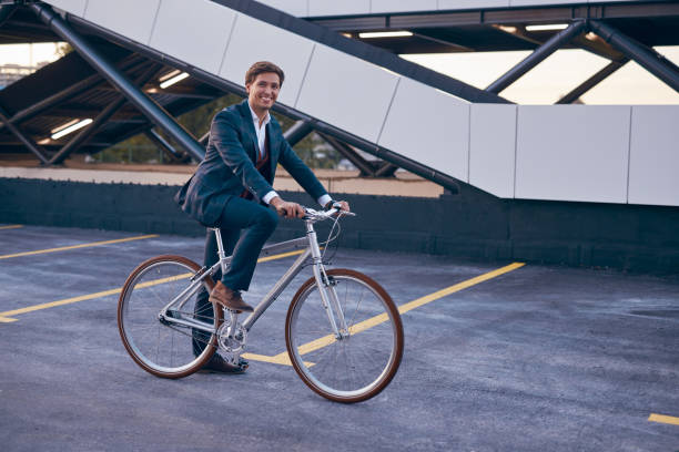 istock Happy young man in formal suit riding bicycle on street 1303665563