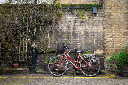 Color image depicting a red pedal bicycle parked on a cobblestone street in London. Plenty of room for copy space.