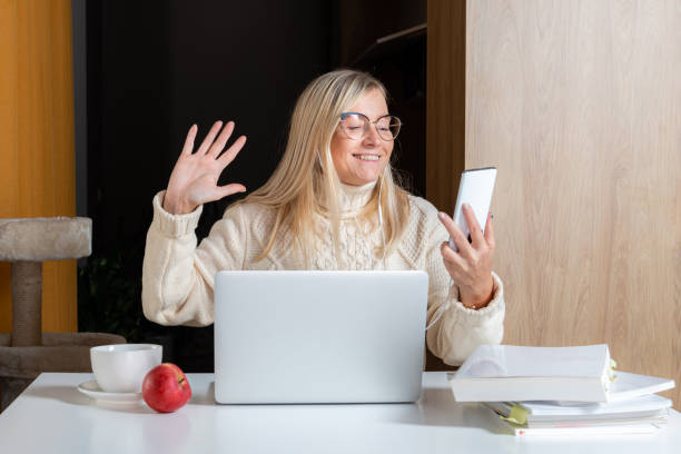 istock woman in earphones using cellphone while working with laptop at home kitchen 1303671478
