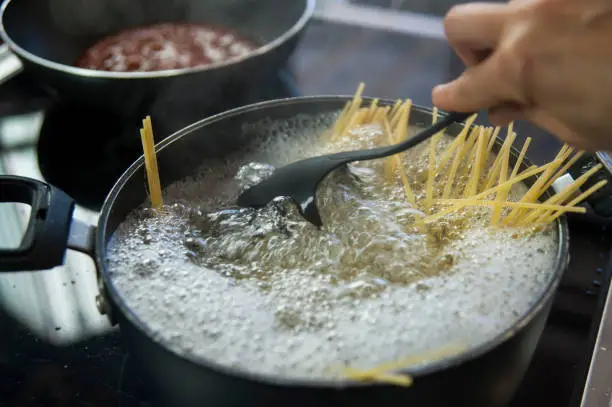 Cooking spaghetti in a pot with boiling water with hand