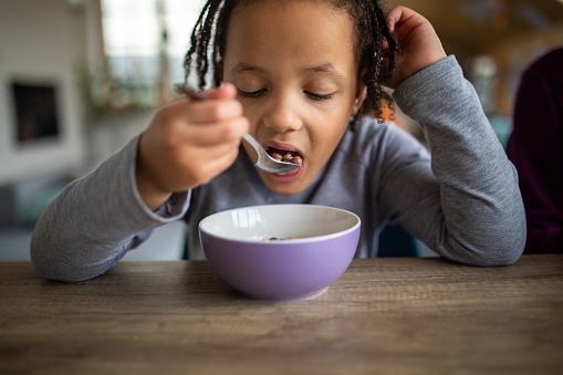 Cute little girl eating cereals for breakfast at dining table