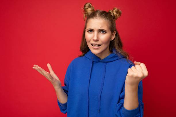 Photo of emotional agressive young beautiful blonde woman with sincere emotions wearing blue pullover isolated over red background with free space and showing fist Photo of emotional agressive young beautiful blonde woman with sincere emotions wearing blue pullover isolated over red background with free space and showing fist. wtf stock pictures, royalty-free photos & images