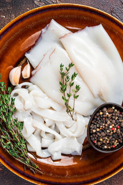istock Sliced raw rings Calamari in a rustic plate with rosemary. Dark background. Top view 1303678210