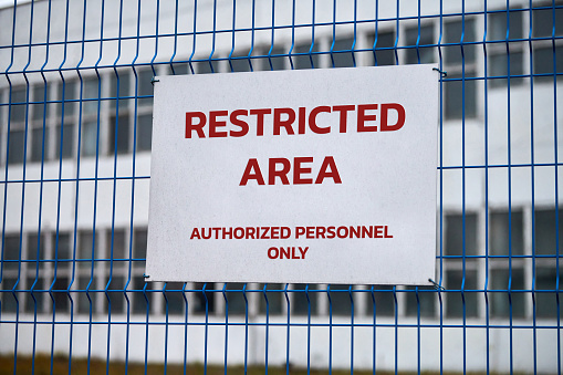 Restricted area, authorized personnel only â safety warning no trespassing sign. Red letters, keep off warning on metal fence, border symbol.