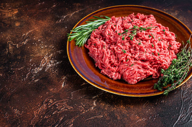 istock Raw ground beef or veal meat on a rustic plate with herbs. Dark background. Top view. Copy space 1303679400