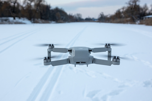 Kharkiv, Ukraine - February 21, 2021: Dji Mavic Mini 2 drone flying in winter snowy landscape in sunset. New quadcopter device hovering. Back view, fly forward above ski track