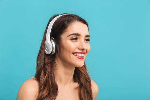 Portrait of a pretty young girl listening to music with headphones isolated over blue background