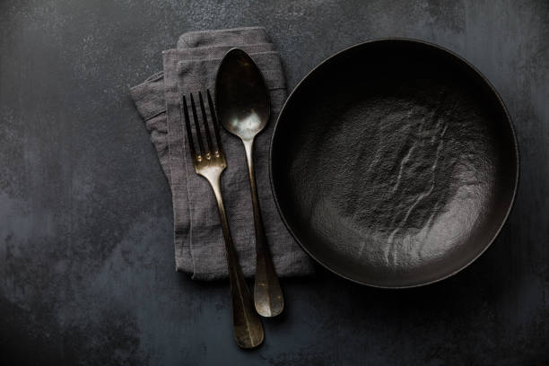istock Table setting with empty black plate, fork and spoon cutlery and linen napkin on dark table 1303682756