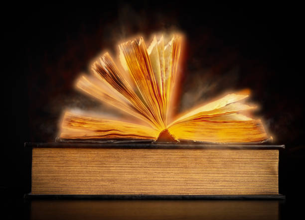 istock open old vintage book on black background, golden haze around 1303685280