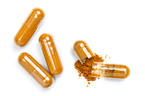 Closeup turmeric herbal powder capsules isolated on white background. Top view. Flat lay.