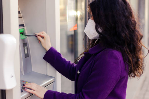 istock Adult woman is using a ATM while wearing mask. 1303686944