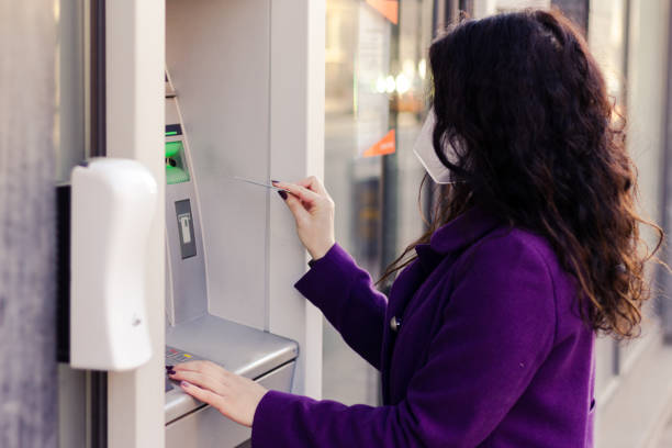 istock Adult woman is using a ATM while wearing mask. 1303687005