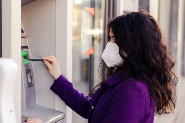 istock Adult woman is using a ATM while wearing mask. 1303687165