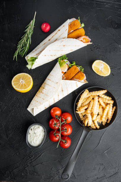 istock Sandwich roll with fish fingers, cheese and vegetables, on black background, top view flat lay 1303687243