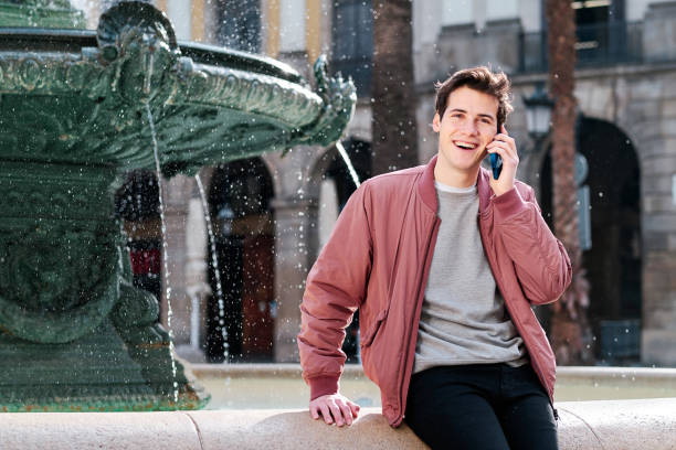 istock Young man smiling while talking on the phone outdoors. 1303687347