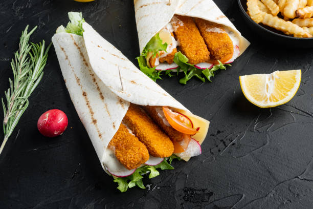 istock Tortilla roll with fish fingers, cheese and vegetables, on black background , with copyspace  and space for text 1303688184