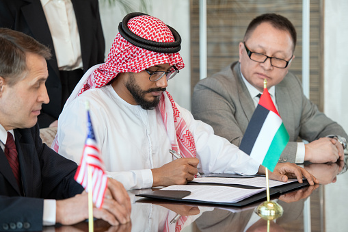 Young confident delegate in national Arabian clothes signing contract of business partnership between UAE and USA after negotiation